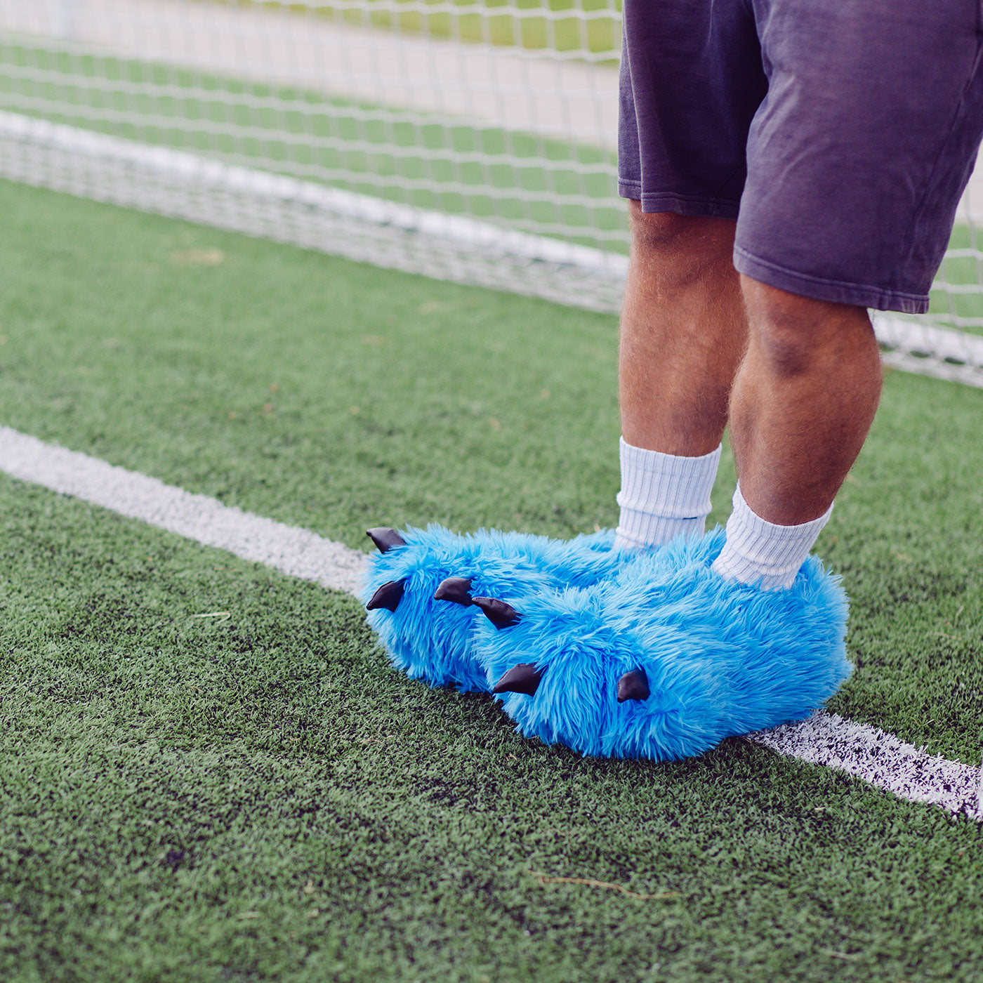 Person mit blauen Tatzeh Hausschuhen auf Fußballfeld