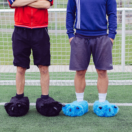 Zwei Personen tragen Tatzenhausschuhe auf Fußballfeld